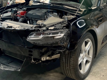 Damaged black car with front-end crash damage in a garage