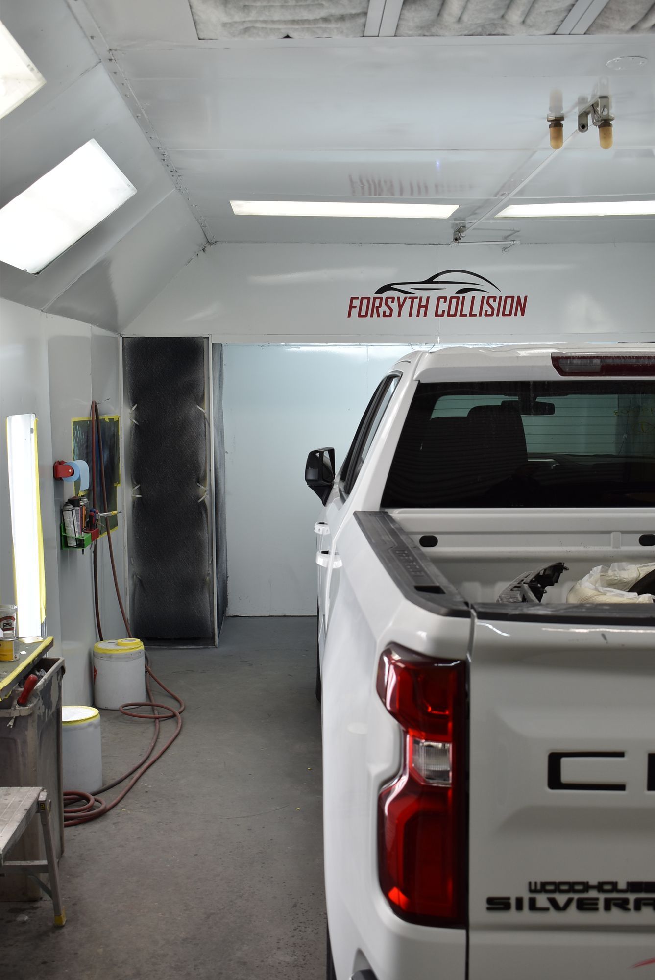 White pickup truck in a bright auto body shop with red equipment and overhead lights