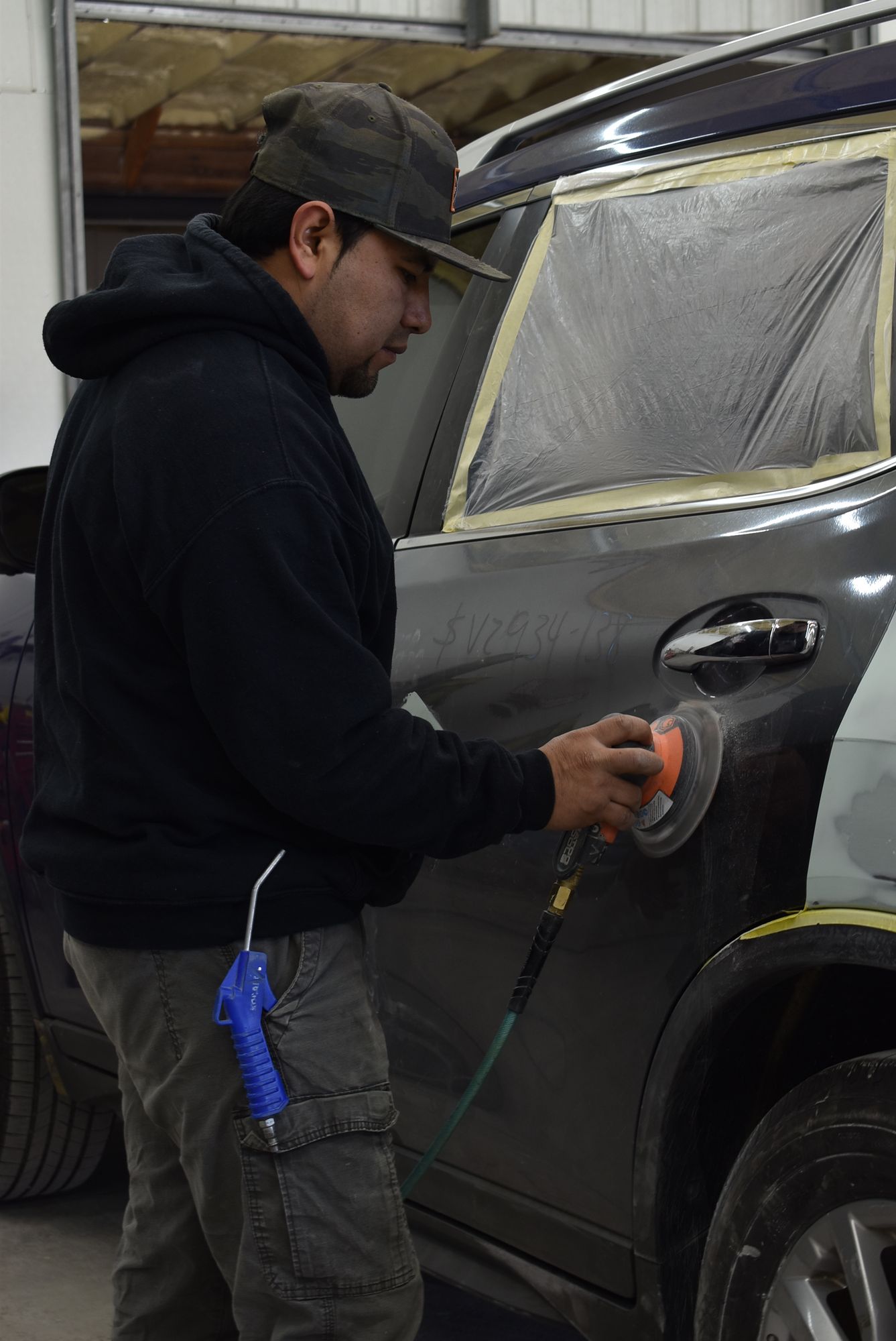 Person polishing the side of a gray SUV with a power buffer in a workshop