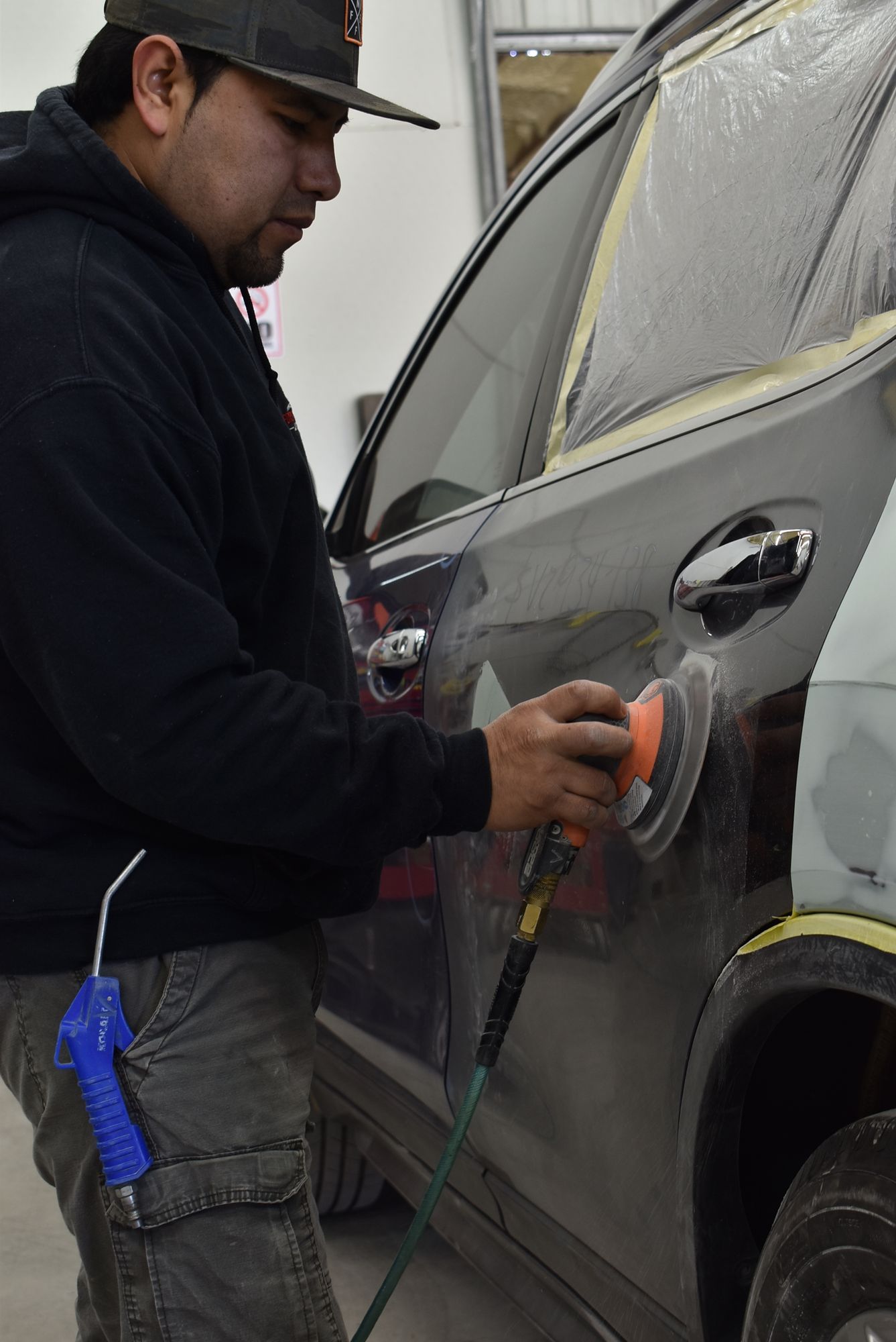 Person using a power sander on a gray car door in a workshop