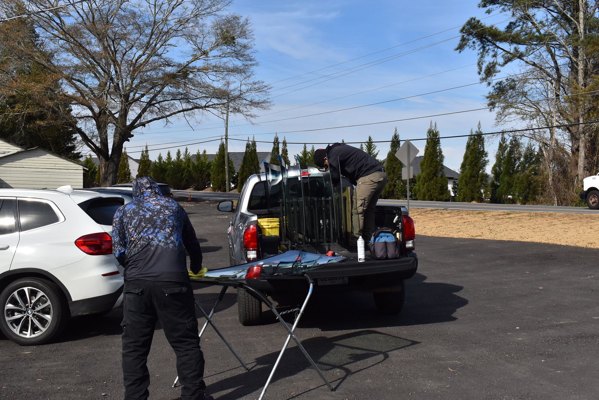Person loading items into a pickup truck beside a white car in a parking lot