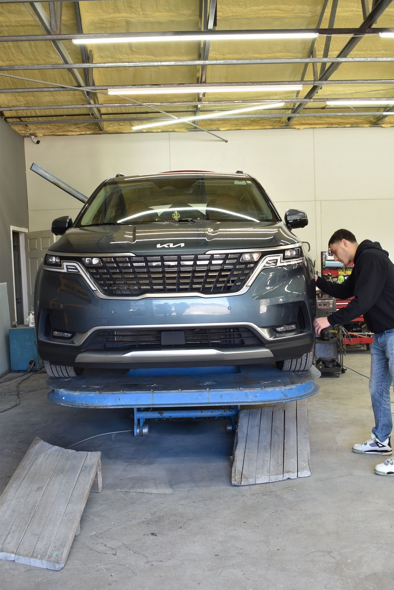 Blue SUV on a lift in a garage, with a mechanic working beside it.