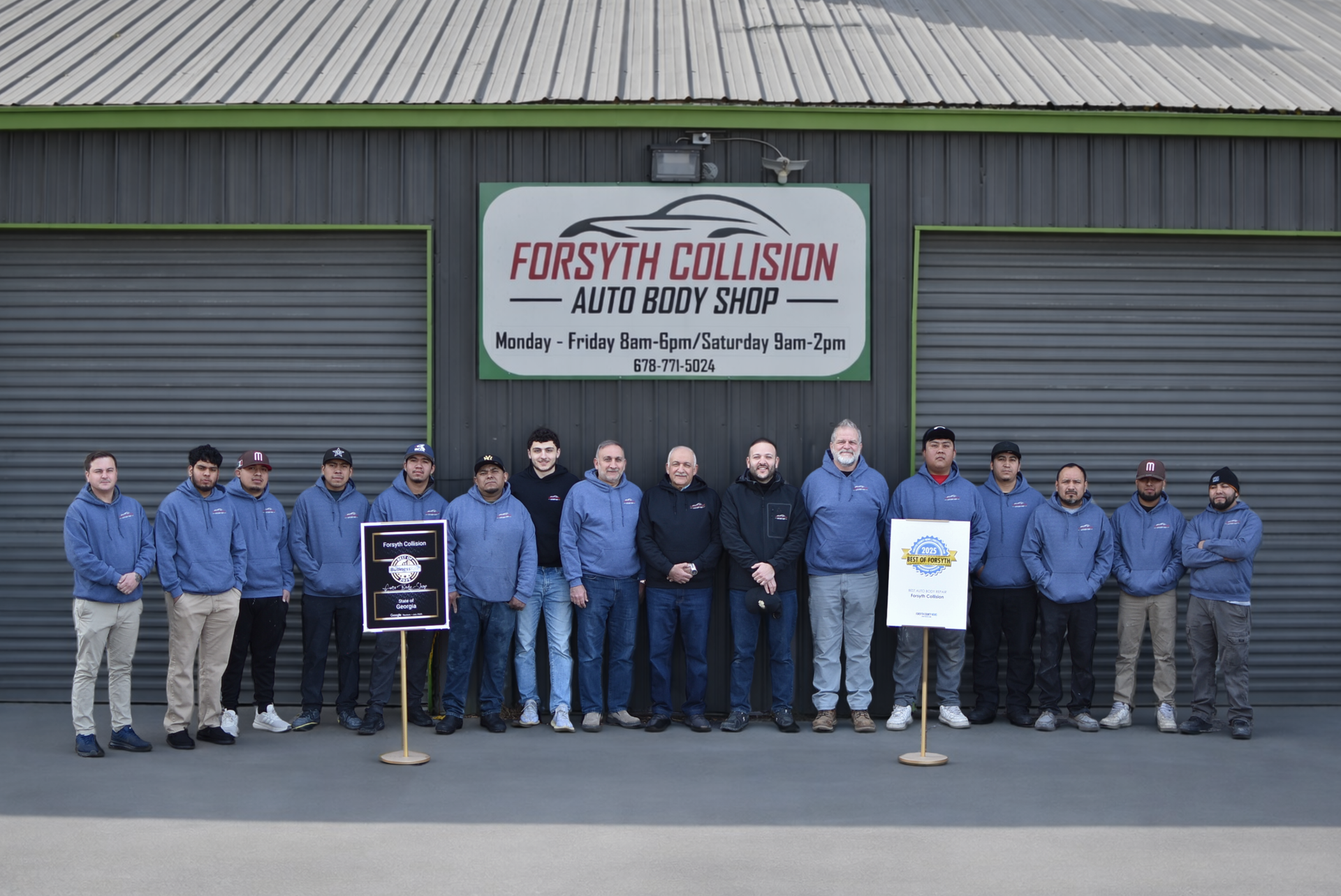 Group of people in blue jackets posing outside Forsyth Collision and Auto Body Shop sign