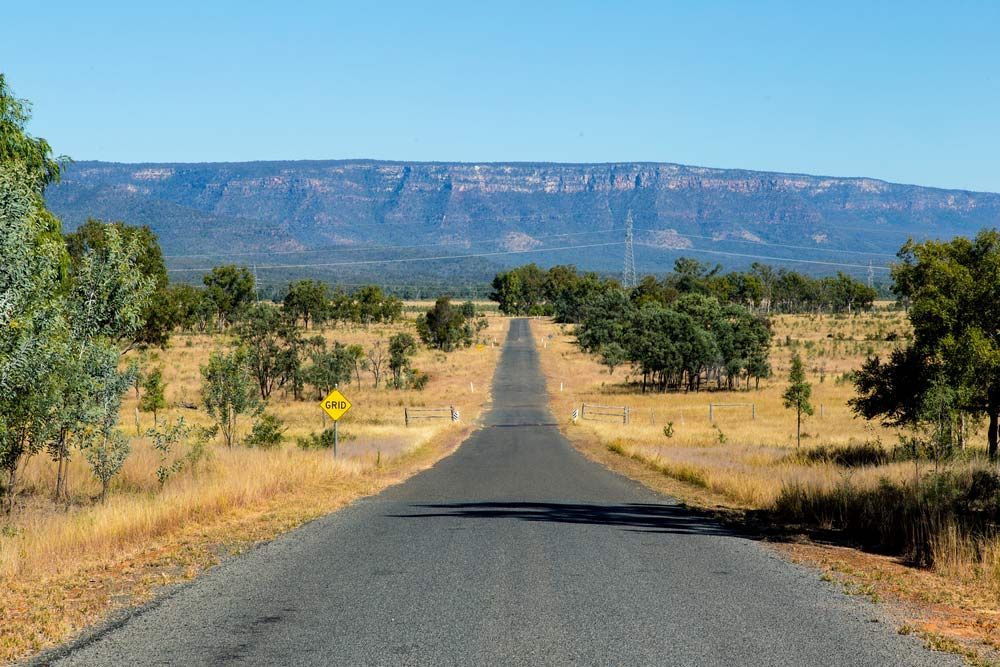 Road Stretches Toward a Distant Dry Grassy Landscape Mountain Range Under a Blue Sky — A1 Loco's Towing in Blackwater, QLD