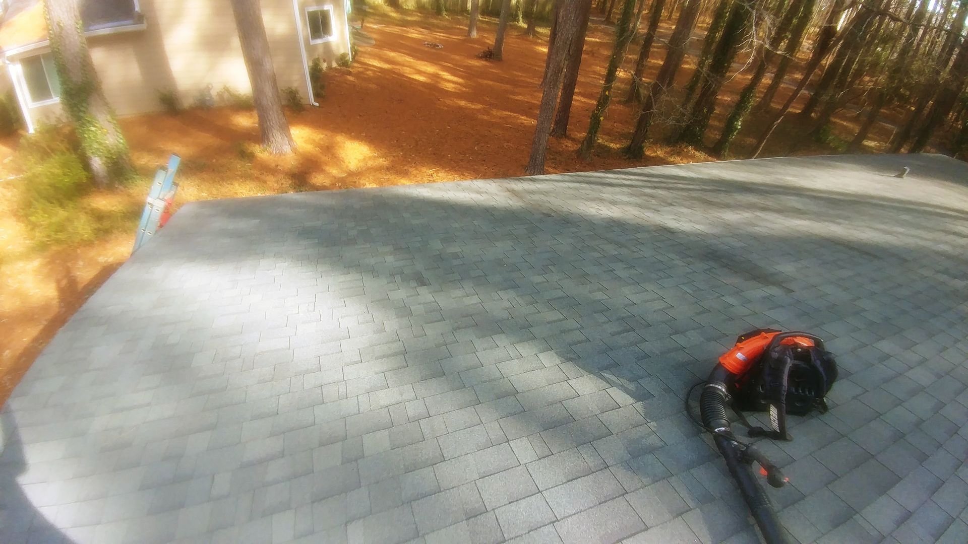A backpack is sitting on top of a roof next to a vacuum cleaner.
