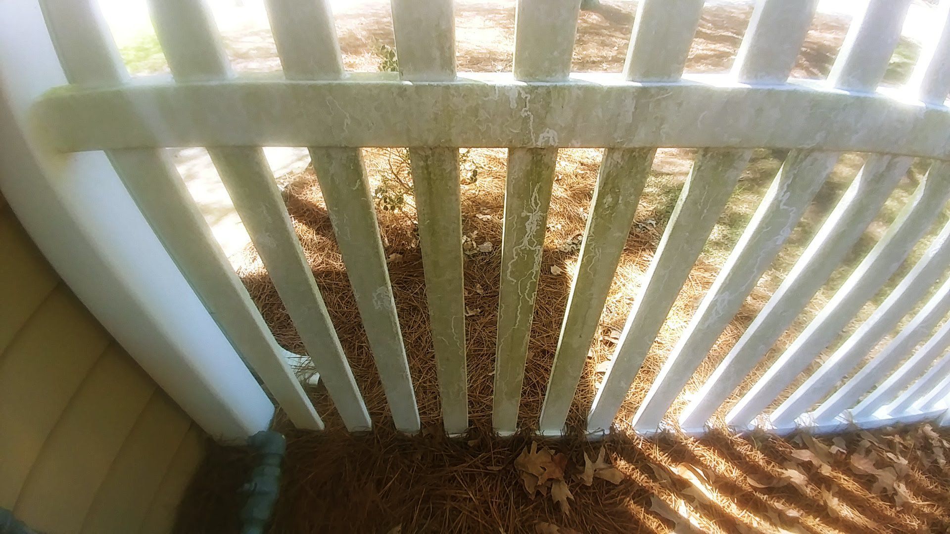 A white picket fence with leaves on the ground behind it.