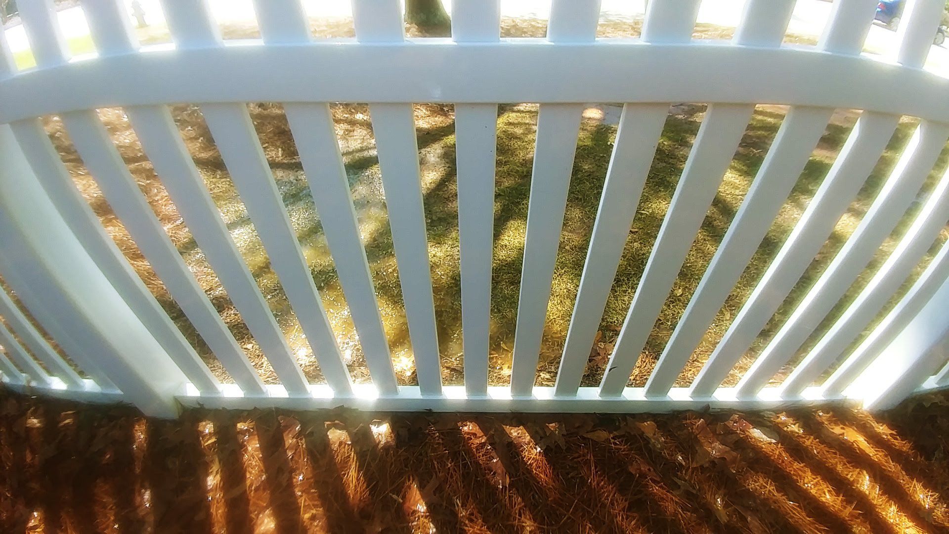 A white fence with a shadow of trees on the ground