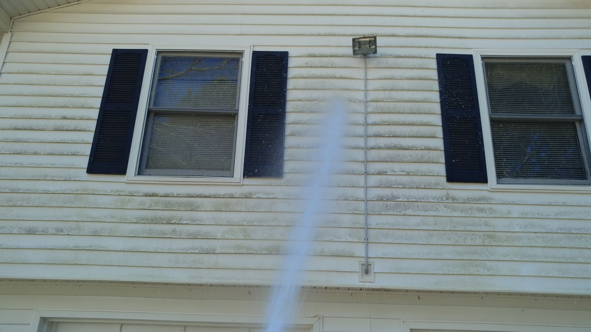 A white house with black shutters is being cleaned with a high pressure washer.