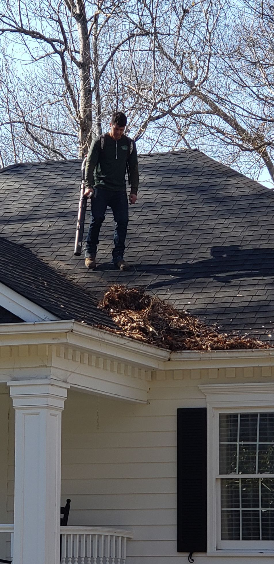 A man is standing on a ladder fixing a gutter on a house.