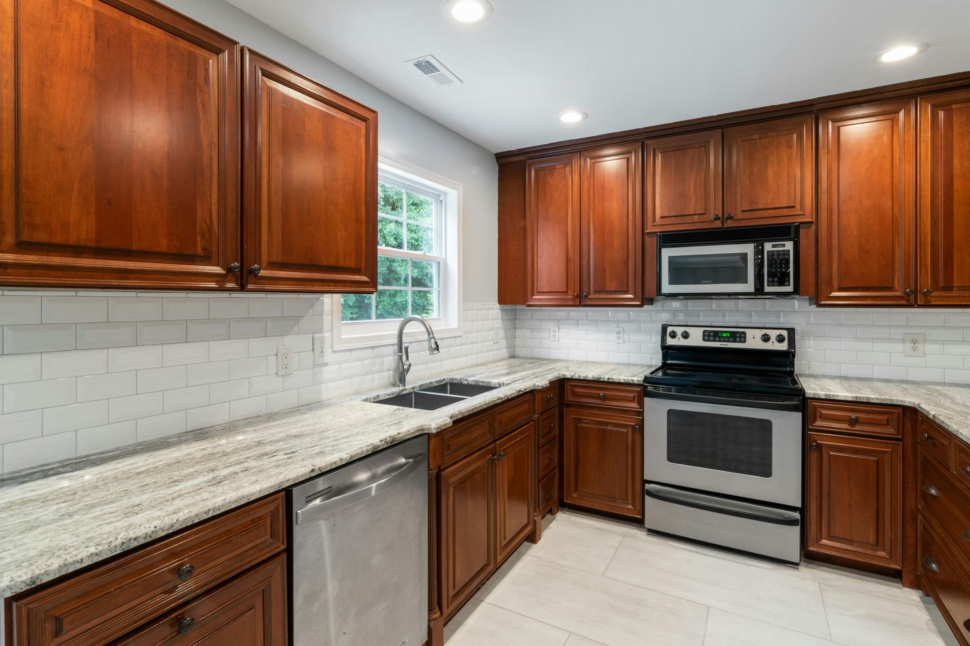 A kitchen with cherry wood cabinets, speckled granite countertops, white subway tile backsplash, and stainless appliances.