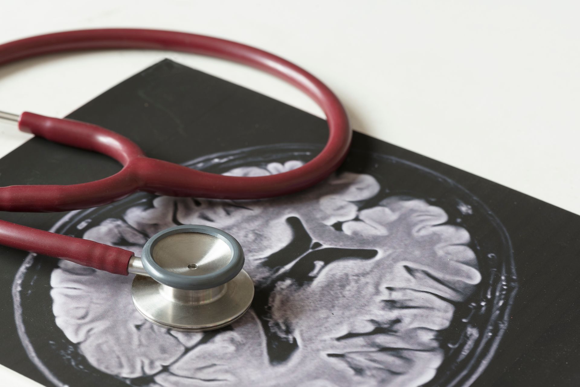 A red stethoscope and picture of human brain MRI, representing neurology surgeon services.