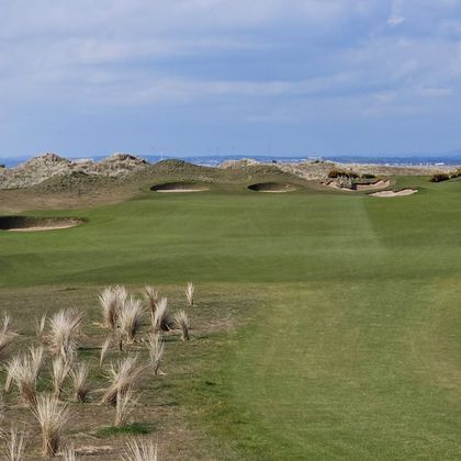 Golf bag on a grassy coastal course with a Scottish flag and the sea in the background