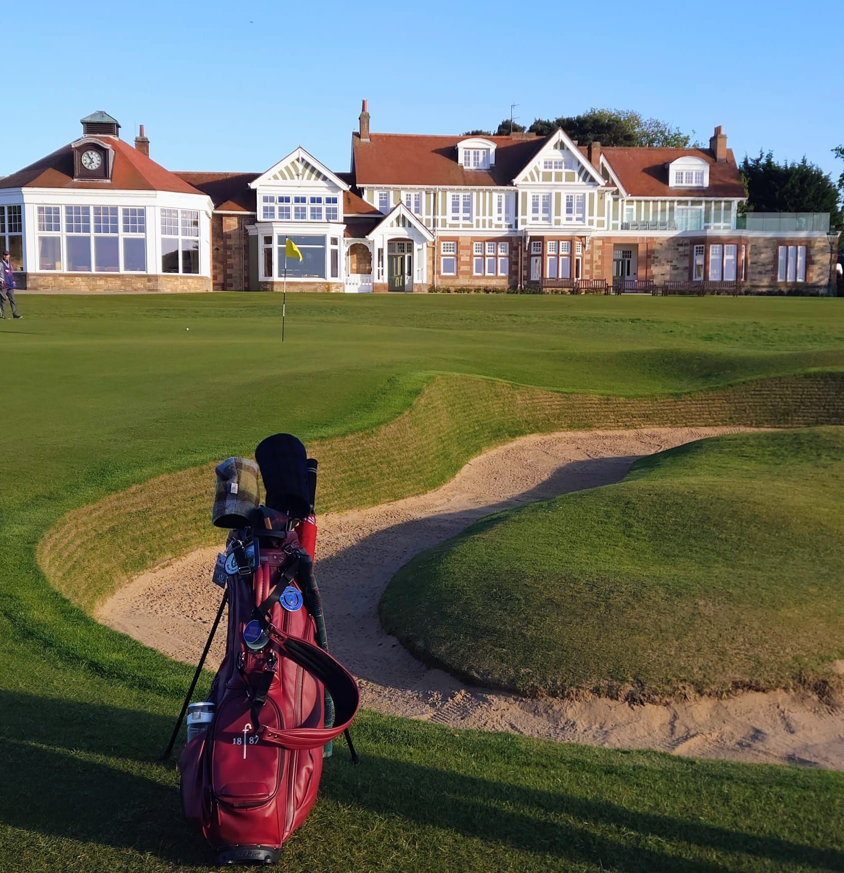 Golf bag on a grassy coastal course with a Scottish flag, ocean in the background.
