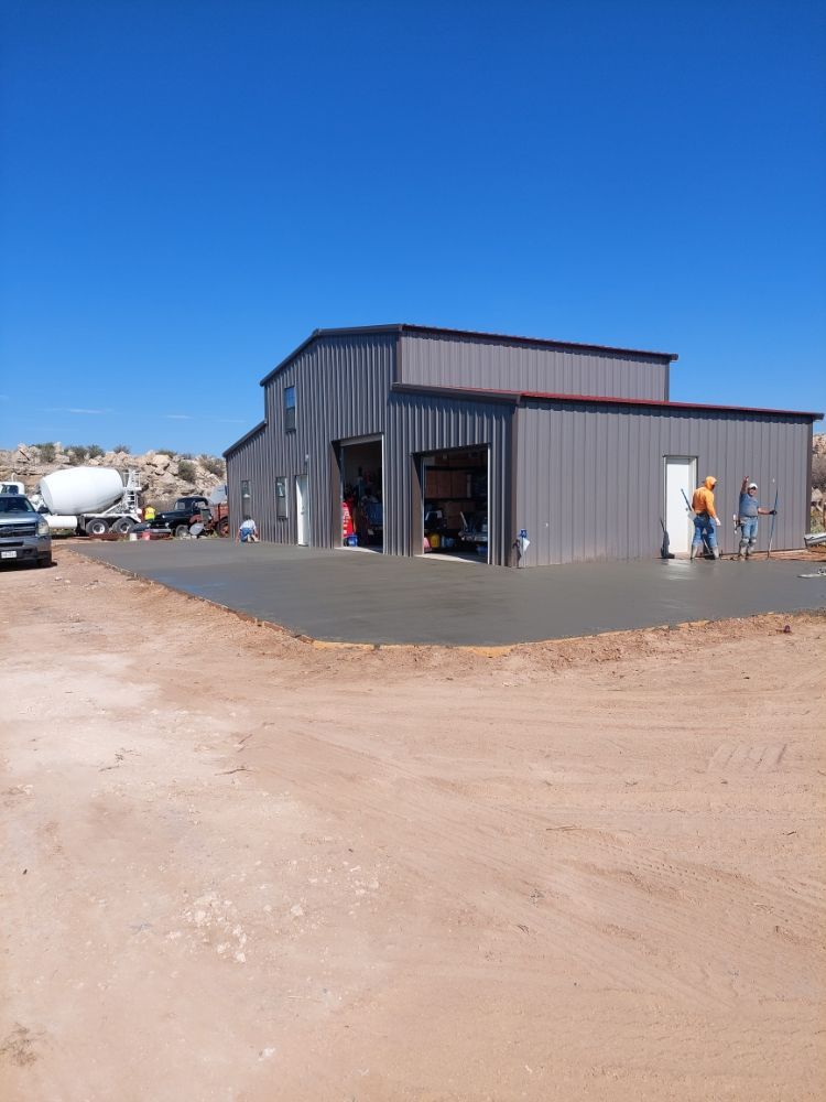 Gray industrial building on a dirt lot, with workers near the open entrance under a clear blue sky.