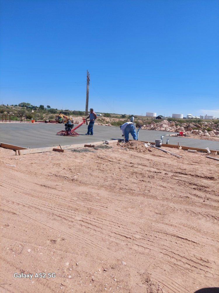 People working on a sandy site near a paved area under a clear blue sky