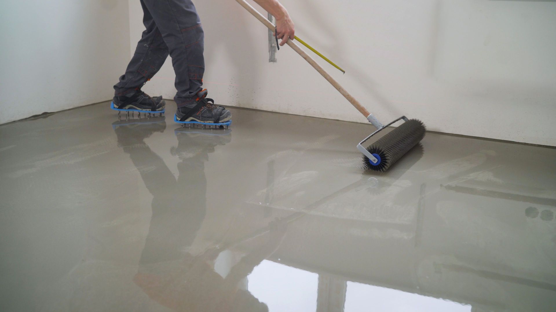 Person rolling gray epoxy on a floor with a paint roller in a room under renovation.