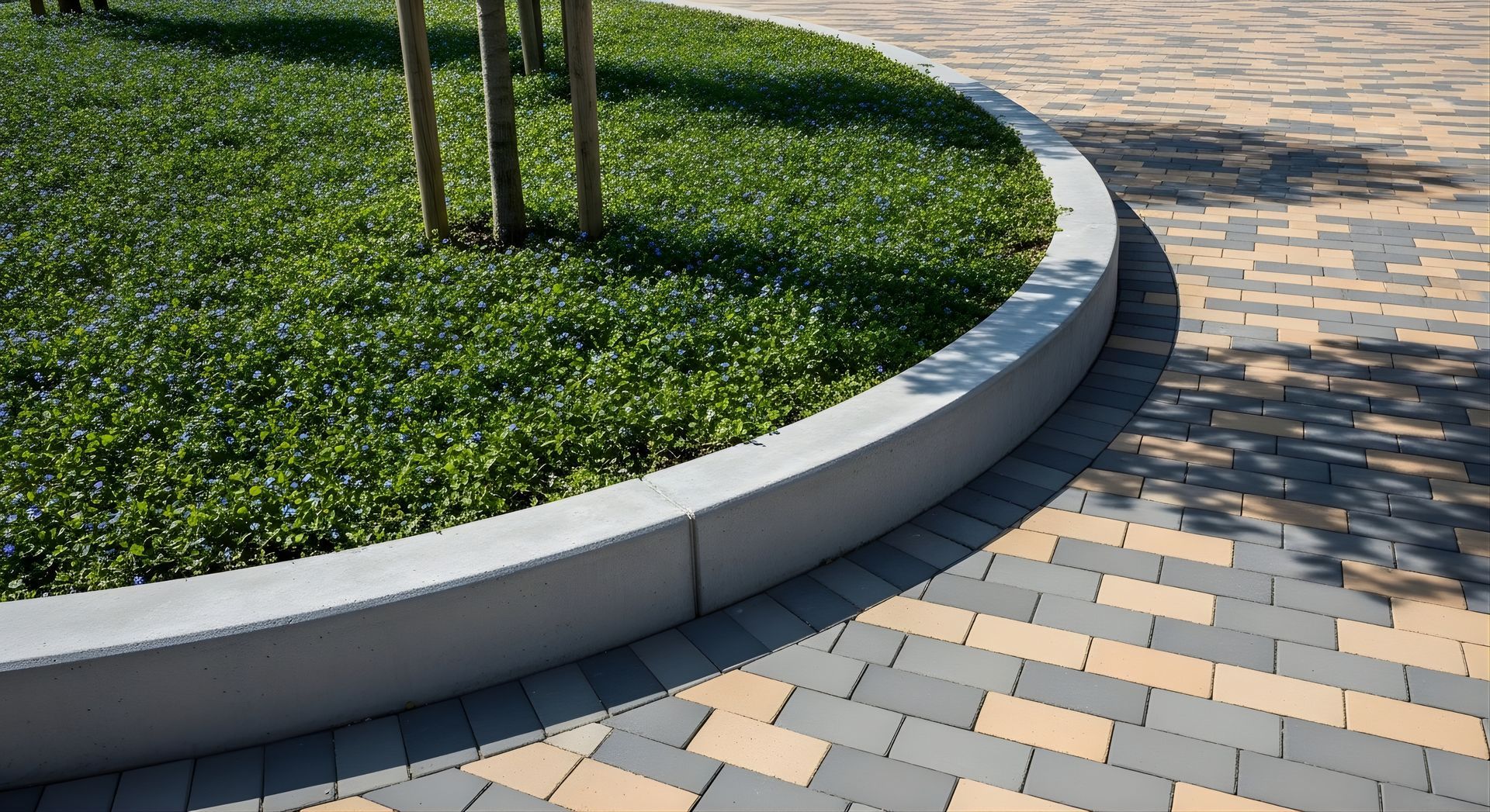 Curved concrete planter with green groundcover beside a patterned brick walkway
