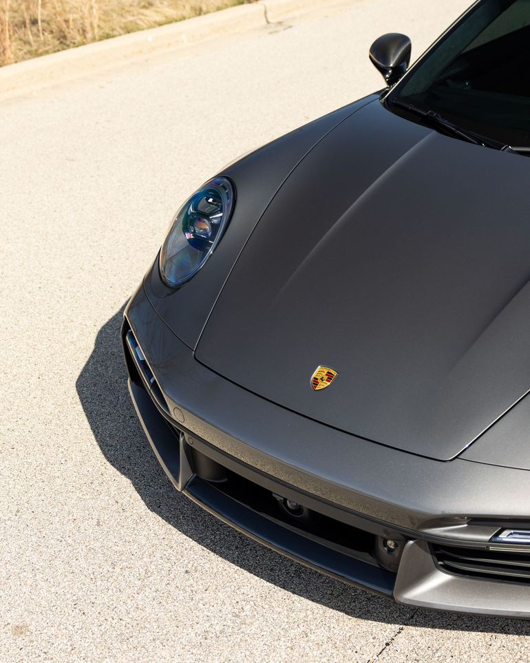Front-left view of a gray Porsche sports car parked on sunlit pavement.