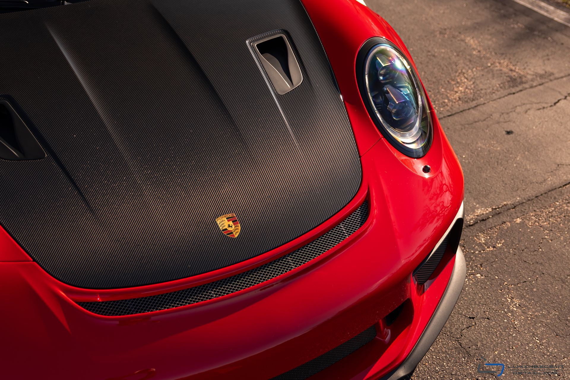 Red Porsche sports car close-up with carbon-fiber hood on pavement