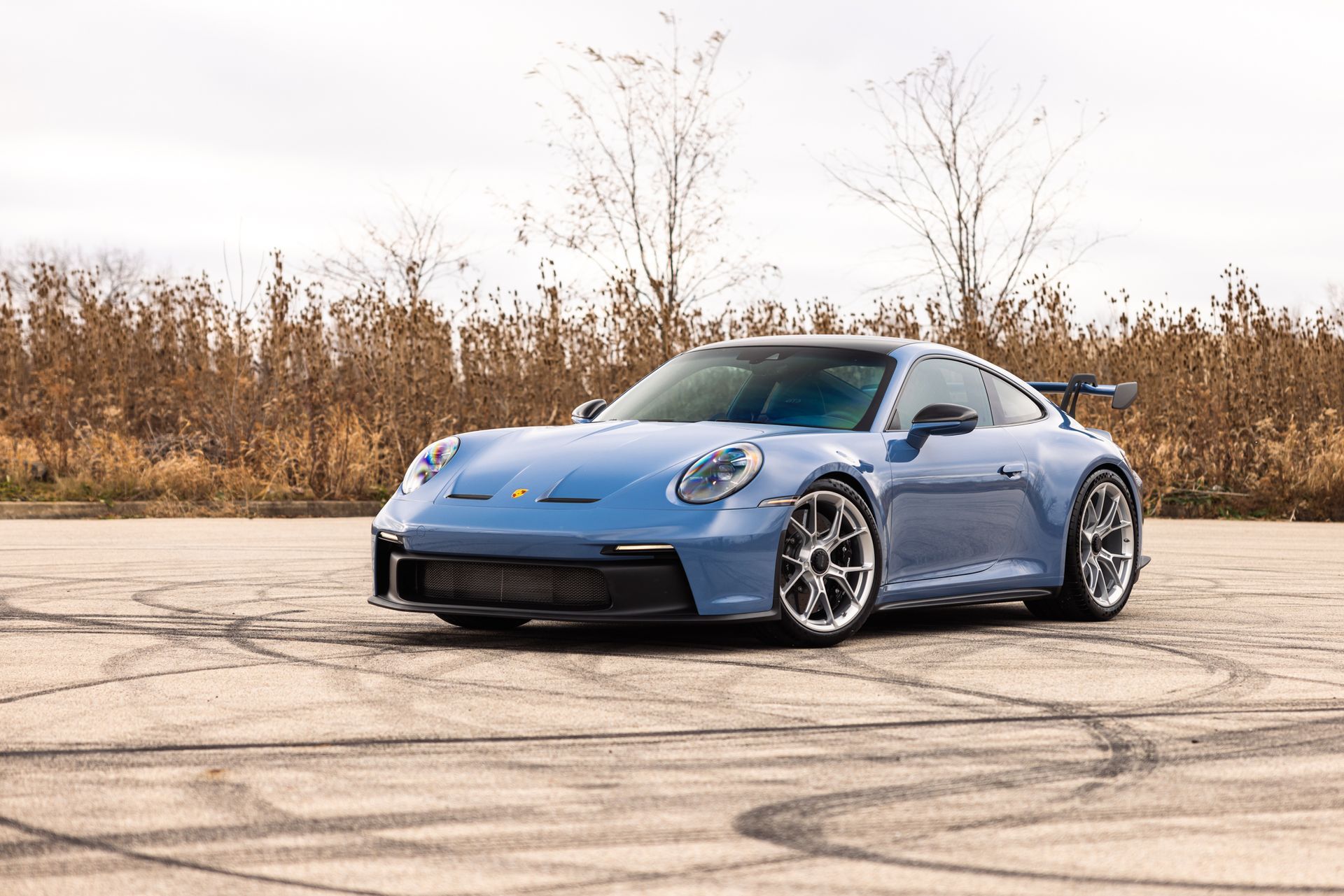 Blue sports car parked on a cracked lot with autumn trees in the background
