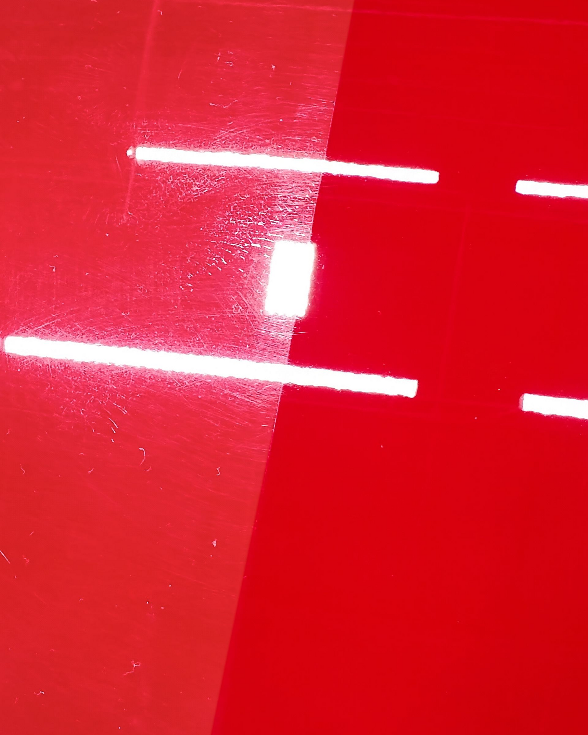 Close-up of a glossy red car surface with bright white reflections and a small white sticker