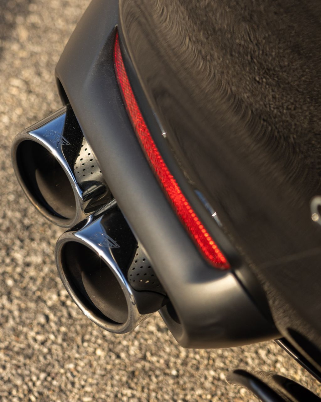 Close-up of a car’s dual chrome exhaust tips beside a red rear reflector