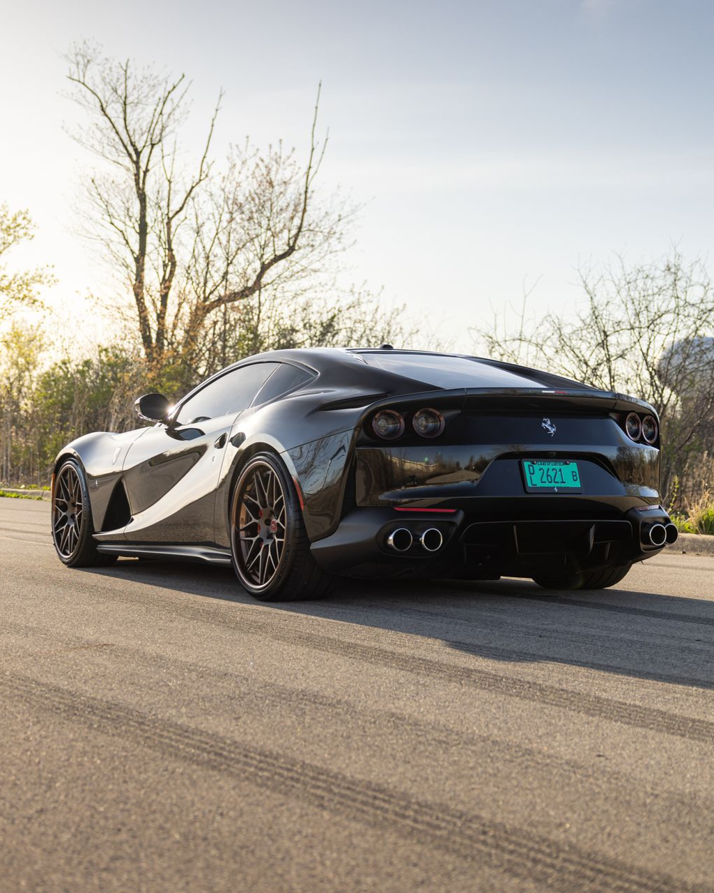 Black sports car parked on a road with trees in the background, rear view