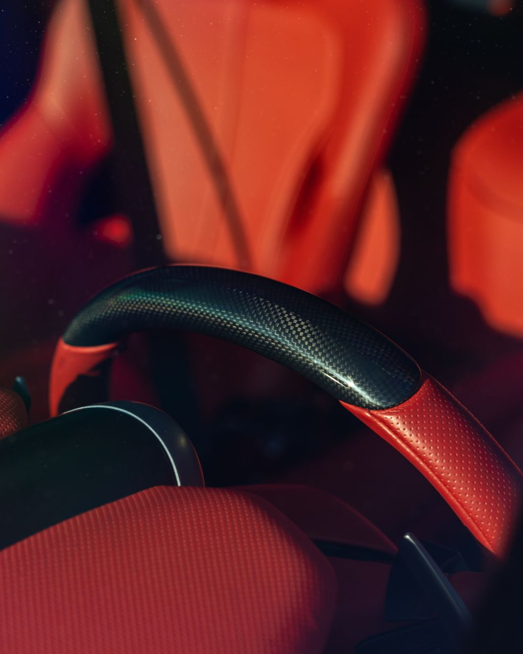 Close-up of a red and black car steering wheel and seat interior lit by warm orange light