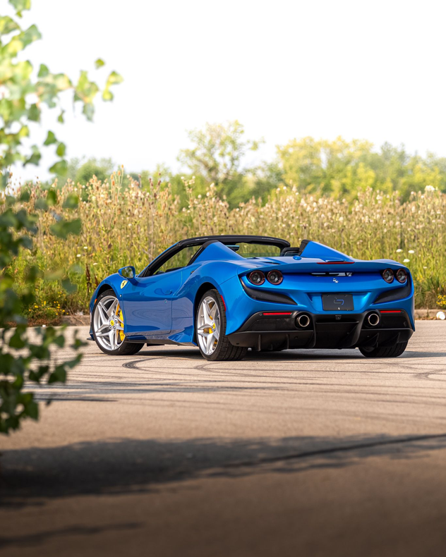 Blue convertible sports car parked on a sunlit road beside tall grass and trees
