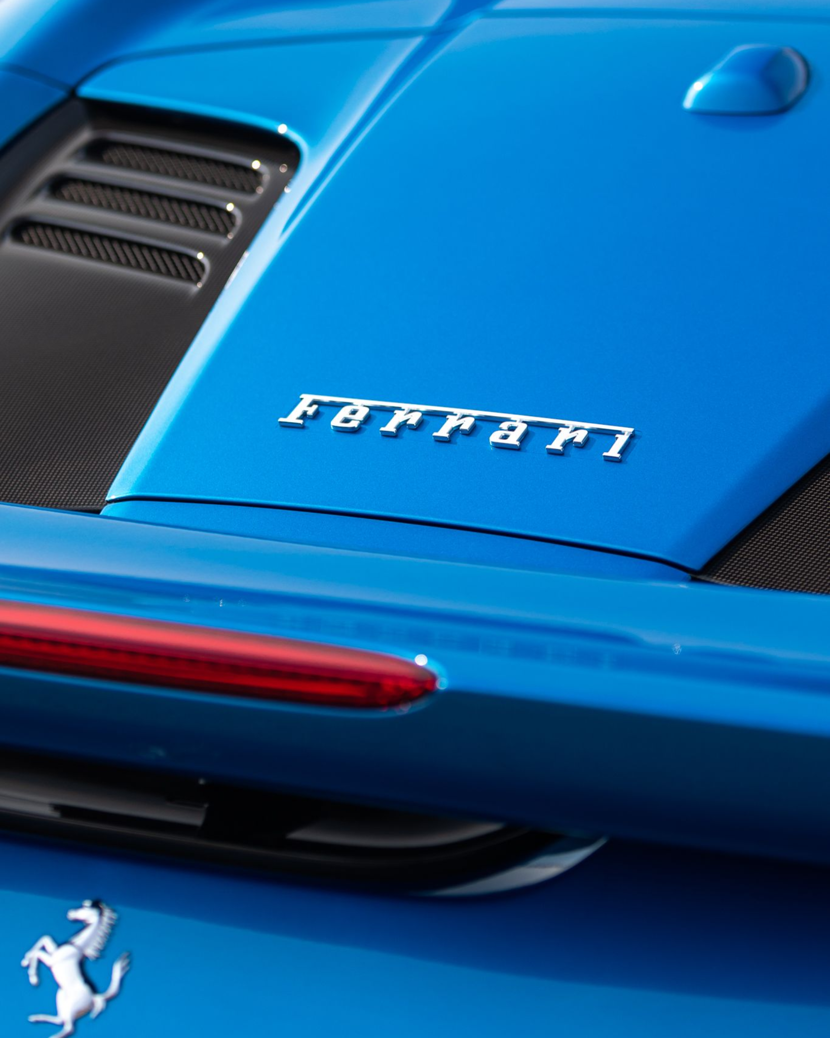 Blue Ferrari rear hood with red taillight and silver badge close-up