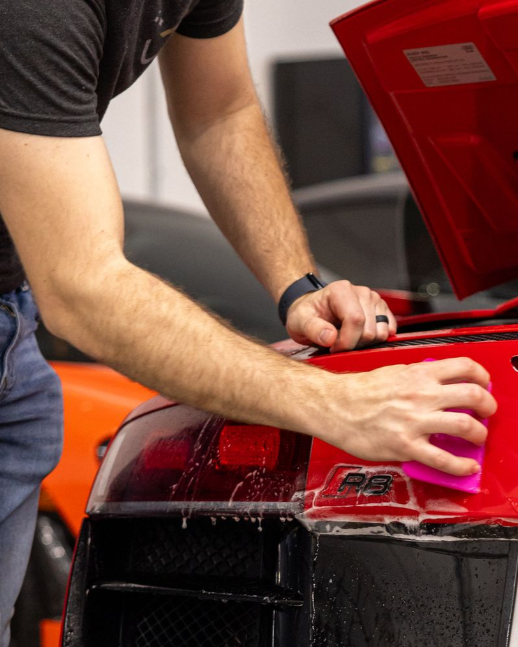 Hands working inside the open hood of a red sports car