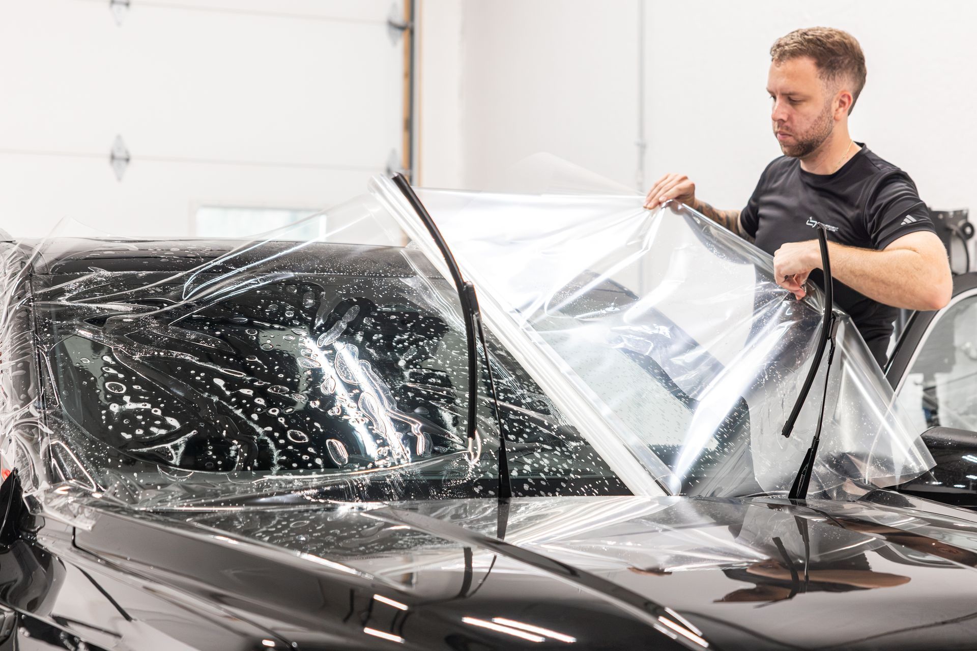Man removing clear protective film from a black car in a garage