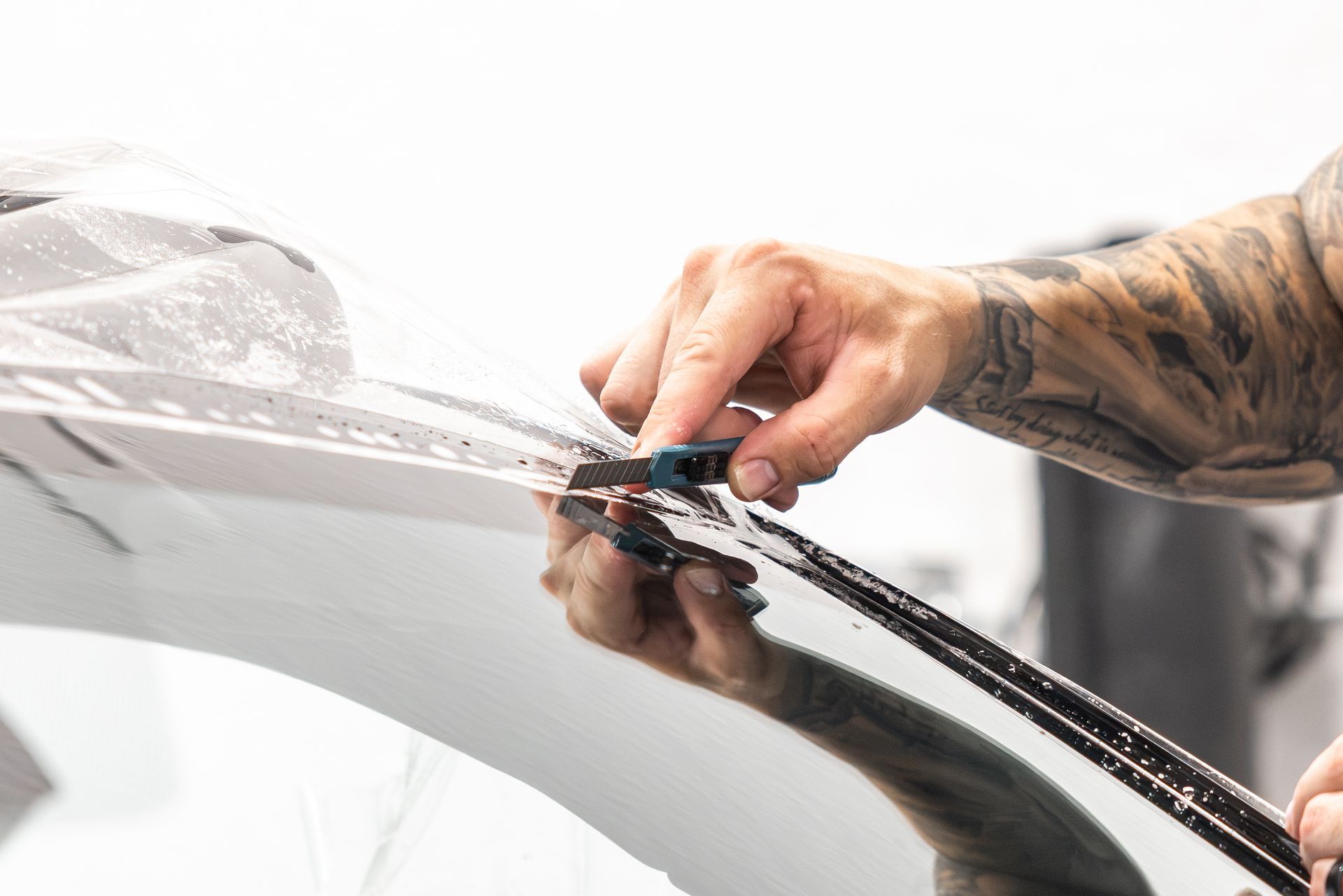 Hand applying black vinyl film to a car windshield with a squeegee