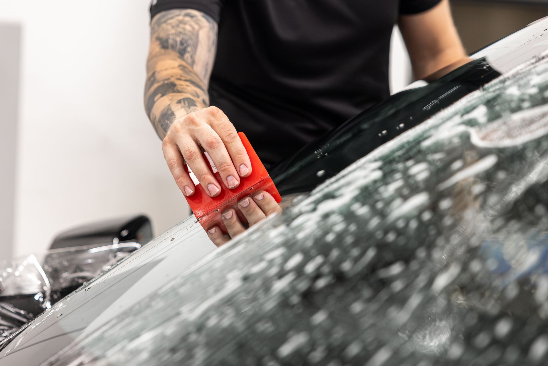 Person wiping a black car windshield with a red cloth during cleaning