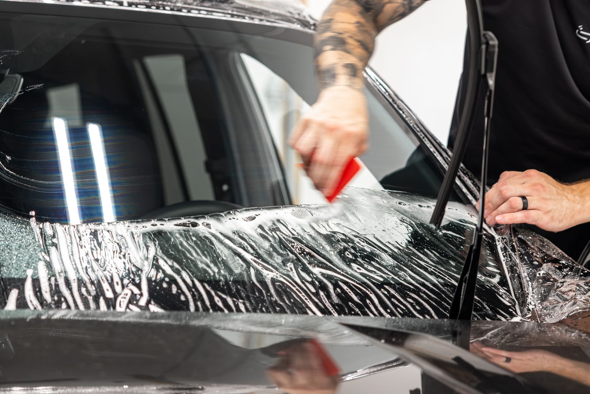 Hands using a blue tool to remove glass from a car windshield in a garage