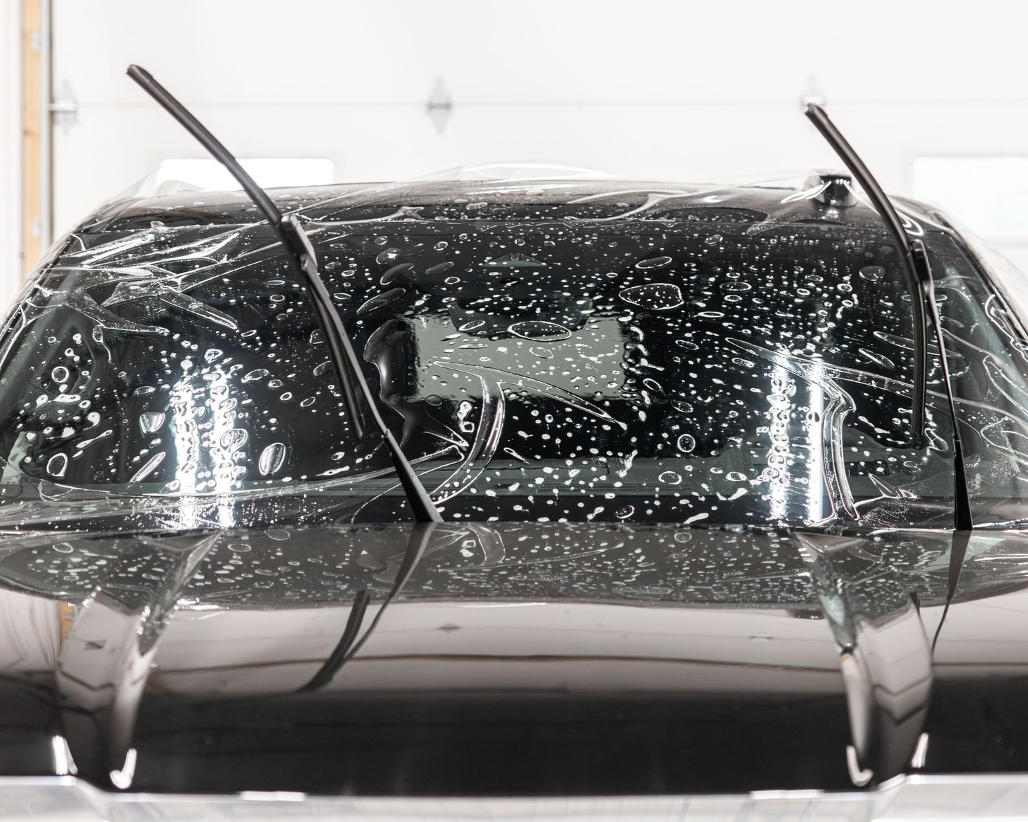 Front view of a black car being washed, covered in soap and water in a car wash tunnel