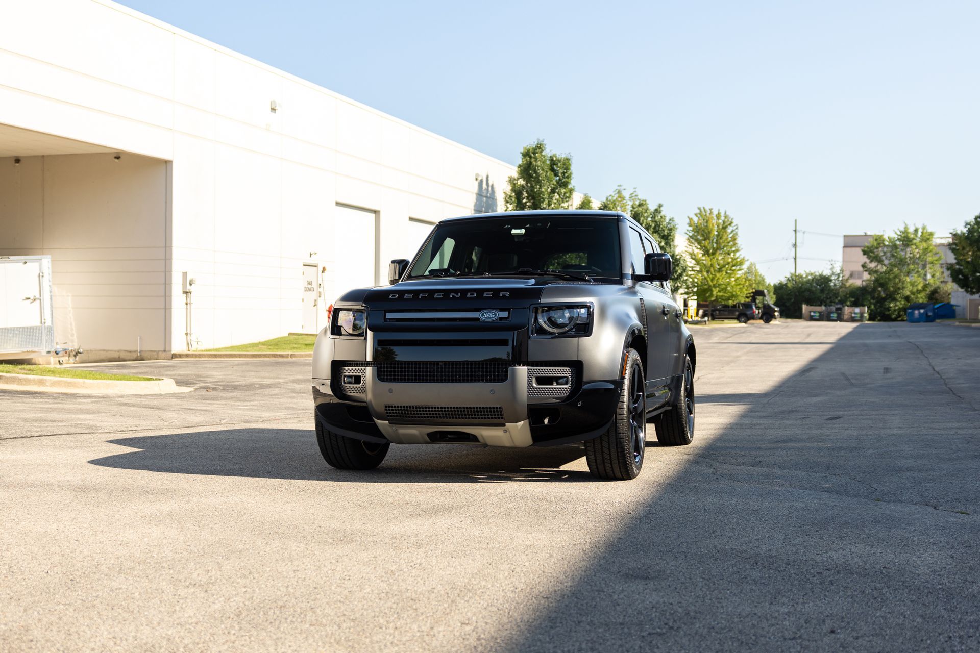 Black off-road SUV parked on a sunlit industrial street near a white warehouse
