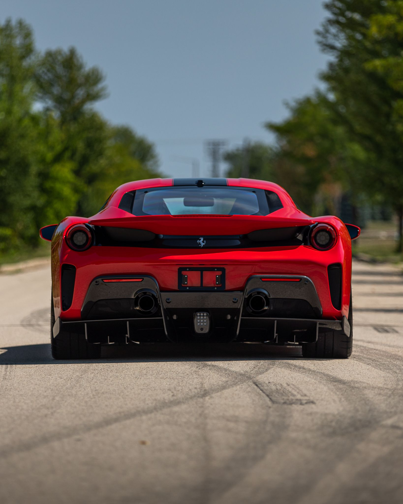 Red sports car driving away on a tree-lined road