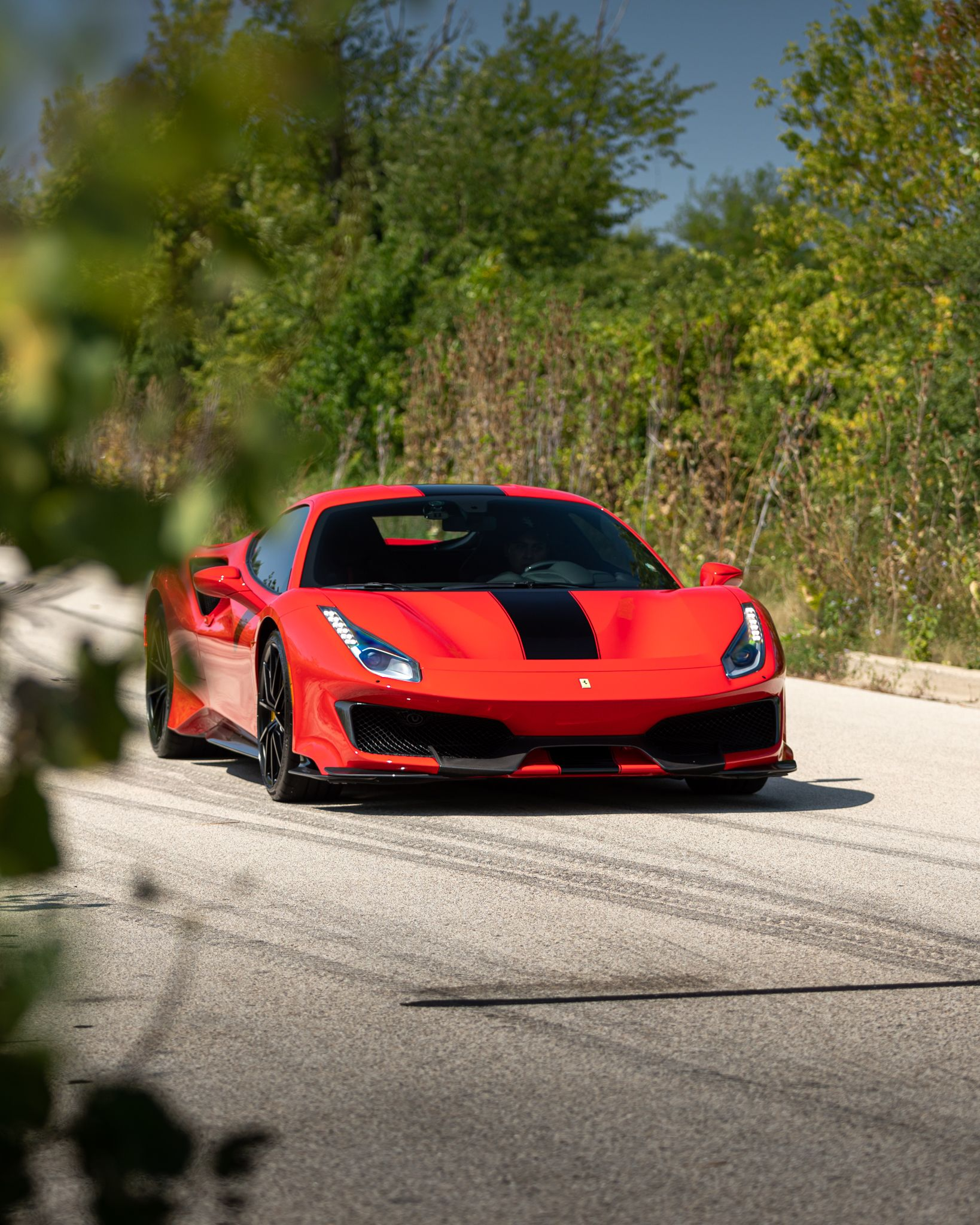 Red sports car driving on a curving road surrounded by green trees