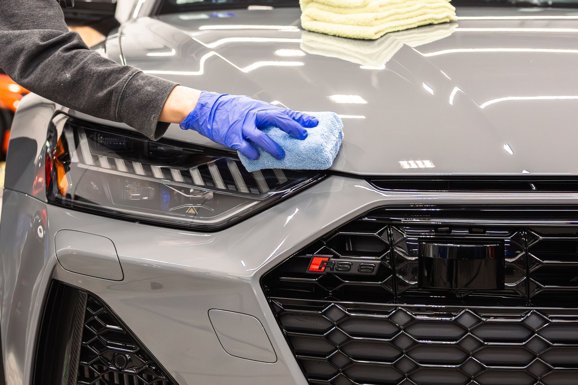 Hand wiping a gray car’s hood with a blue cloth in a garage