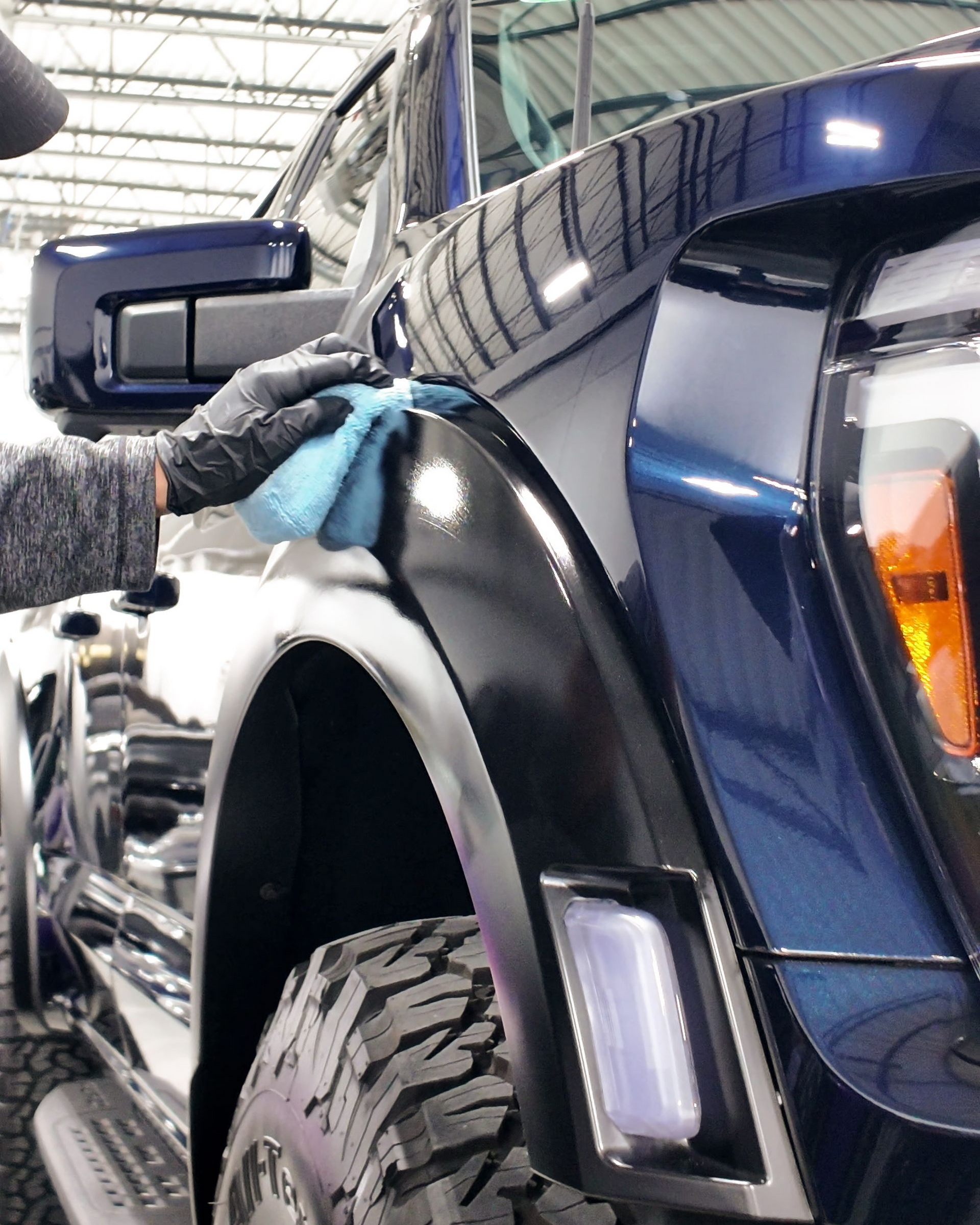 Person polishing a dark blue pickup truck inside a workshop