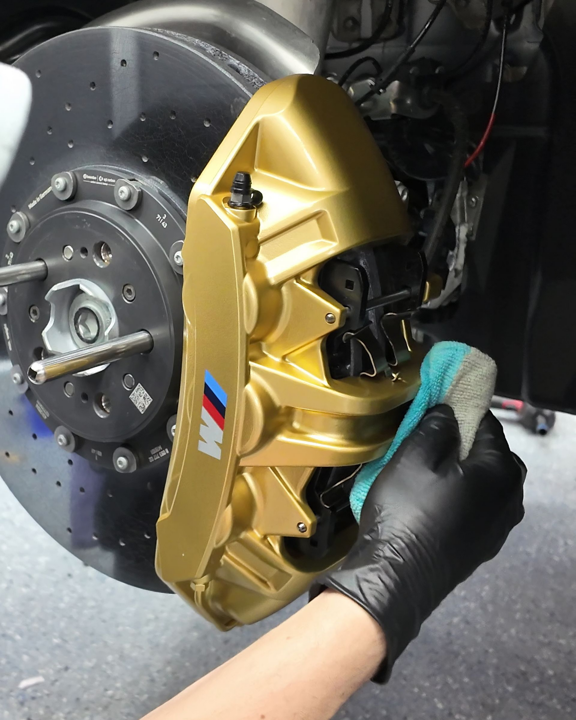 Hand cleaning a gold brake caliper on a car wheel with a teal cloth