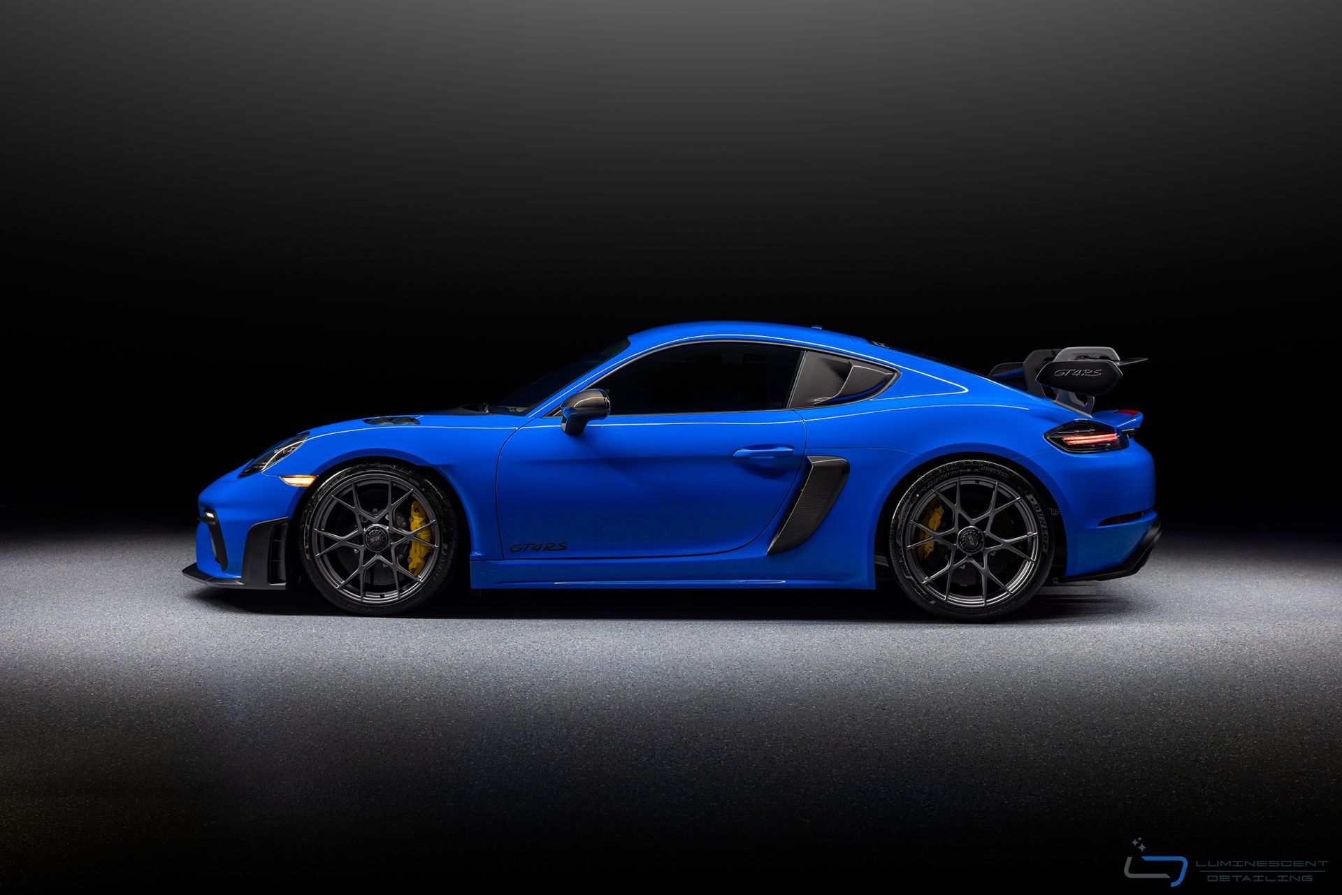 Blue sports car in side view on a dark studio background with black wheels and rear spoiler