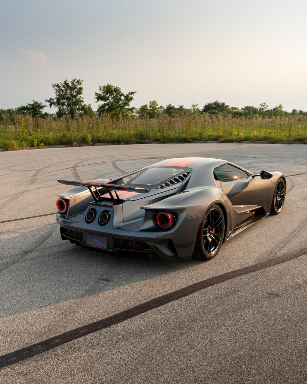 Silver sports car with rear wing on an empty road at sunset, viewed from behind.