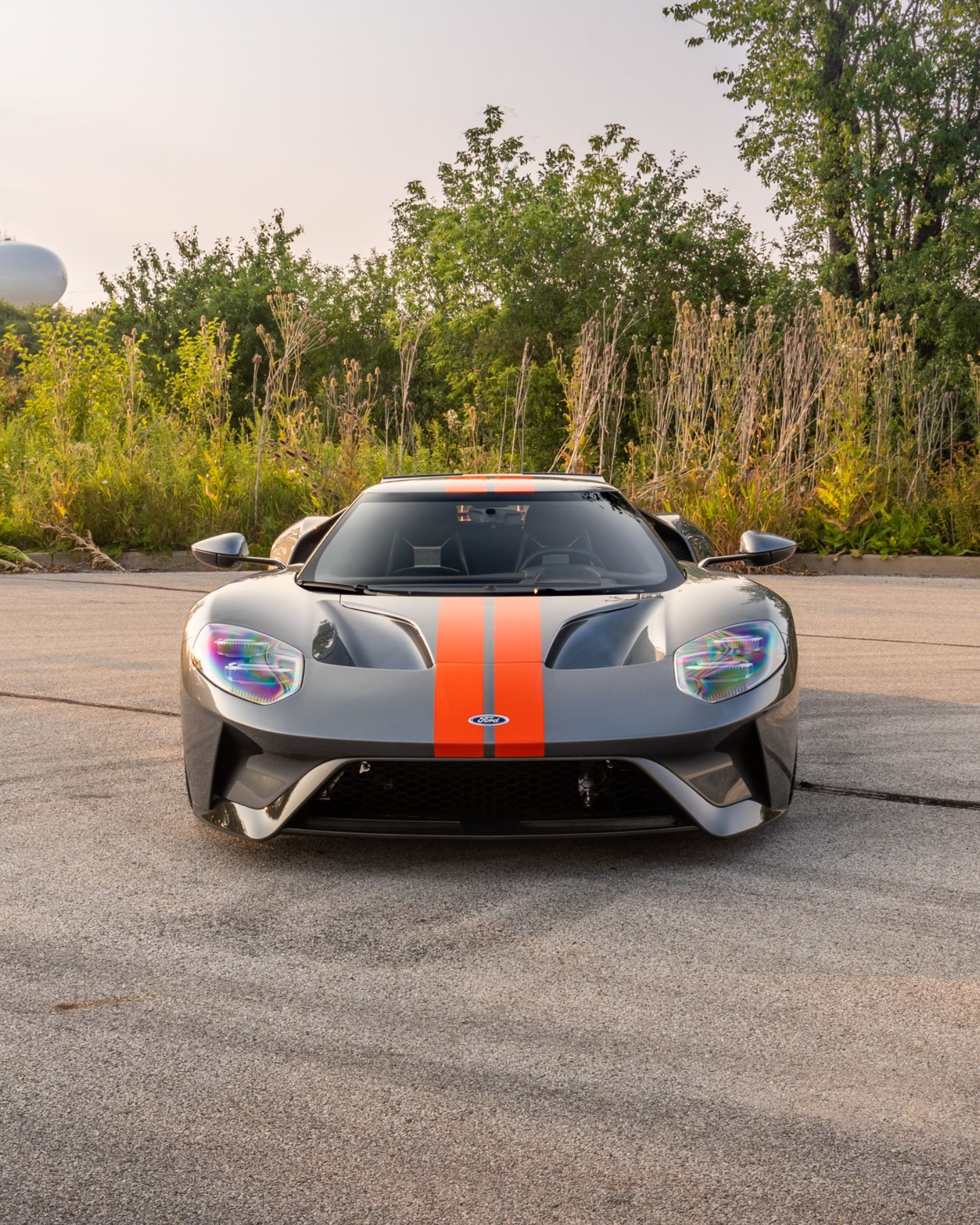 Gray sports car with orange racing stripe parked outdoors at dusk