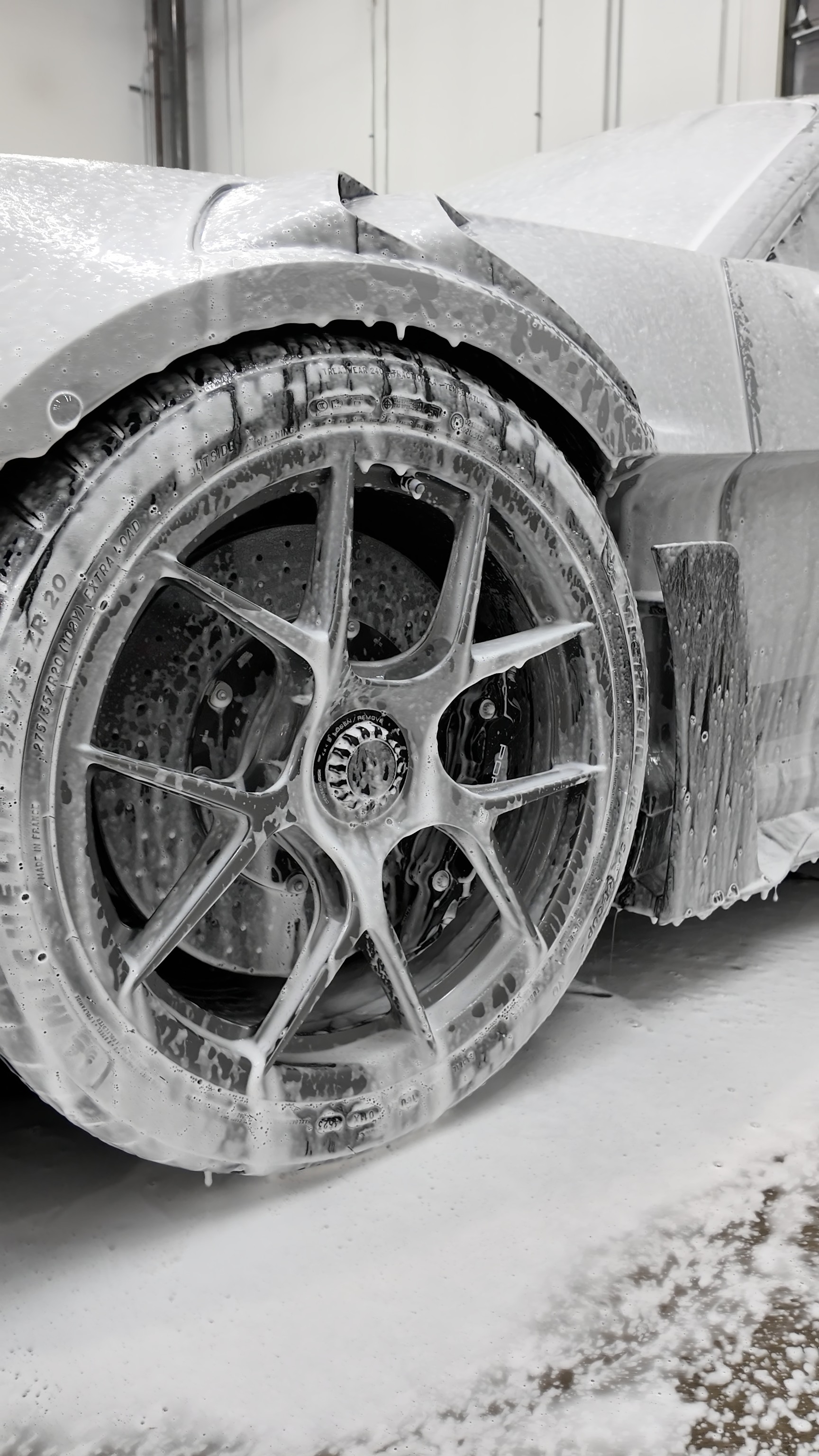 Gloved hand scrubbing a car windshield with soap suds in a close-up view