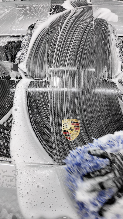 Snow-covered white Porsche with a crest on the hood, parked outdoors in a wintry scene