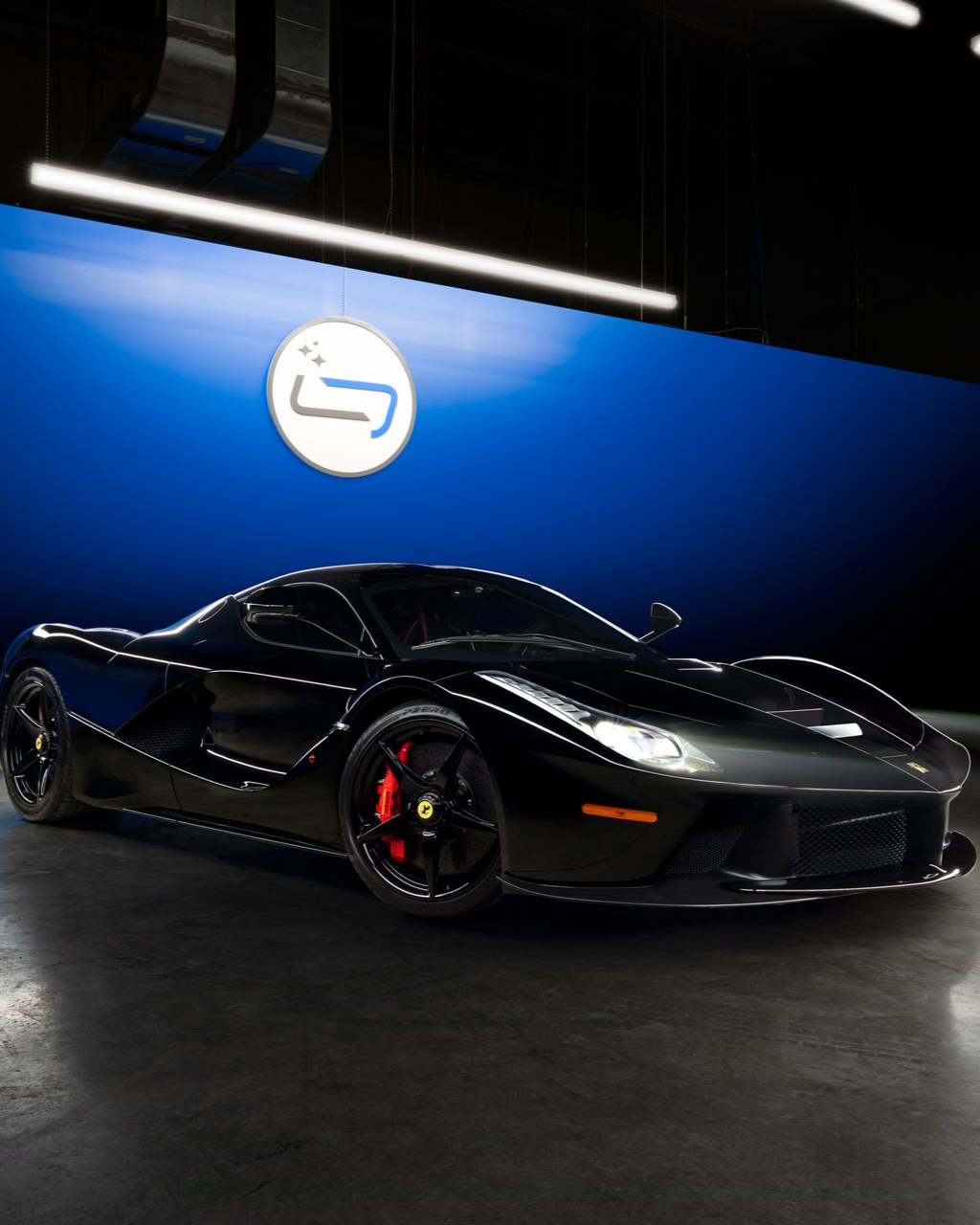 Black sports car with red brake calipers displayed indoors against a blue wall