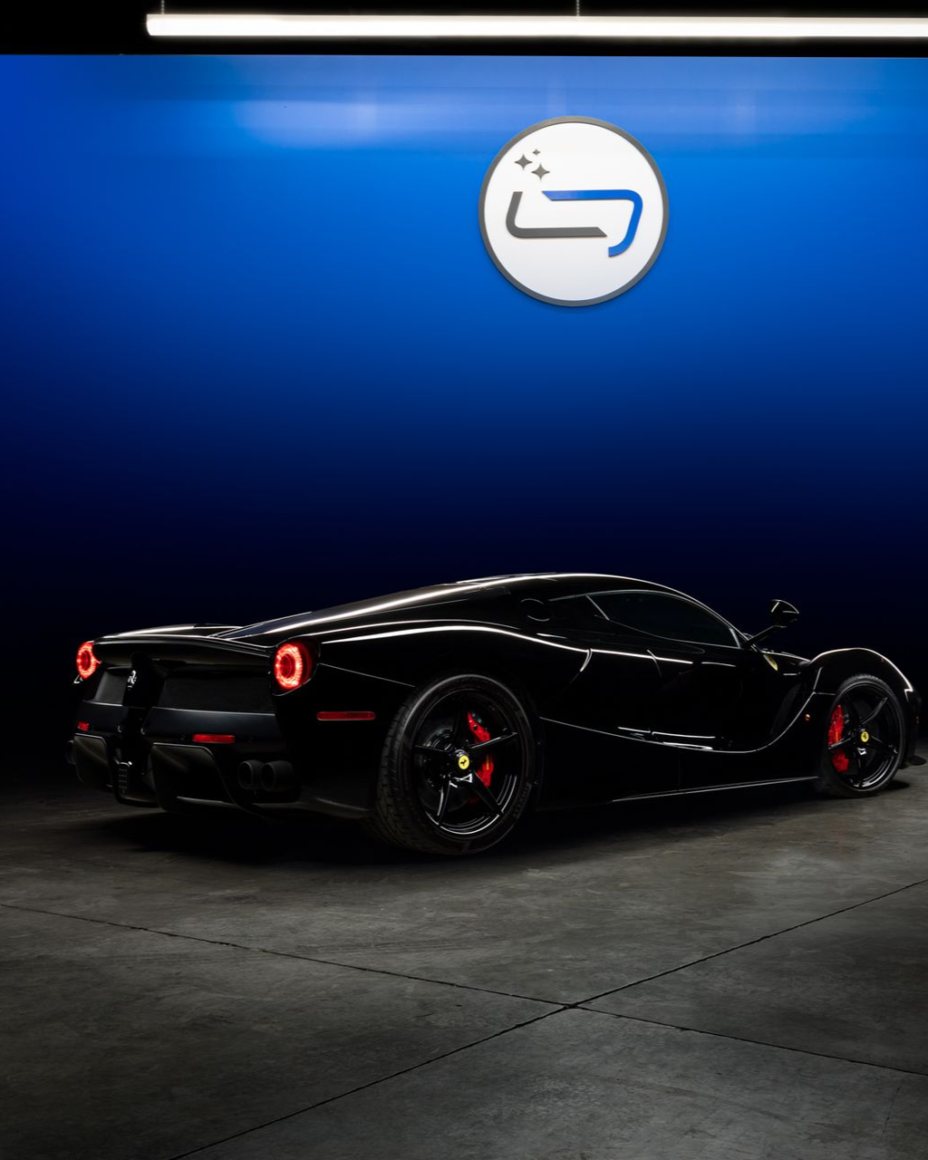 Black sports car in a blue-lit showroom beneath a circular logo