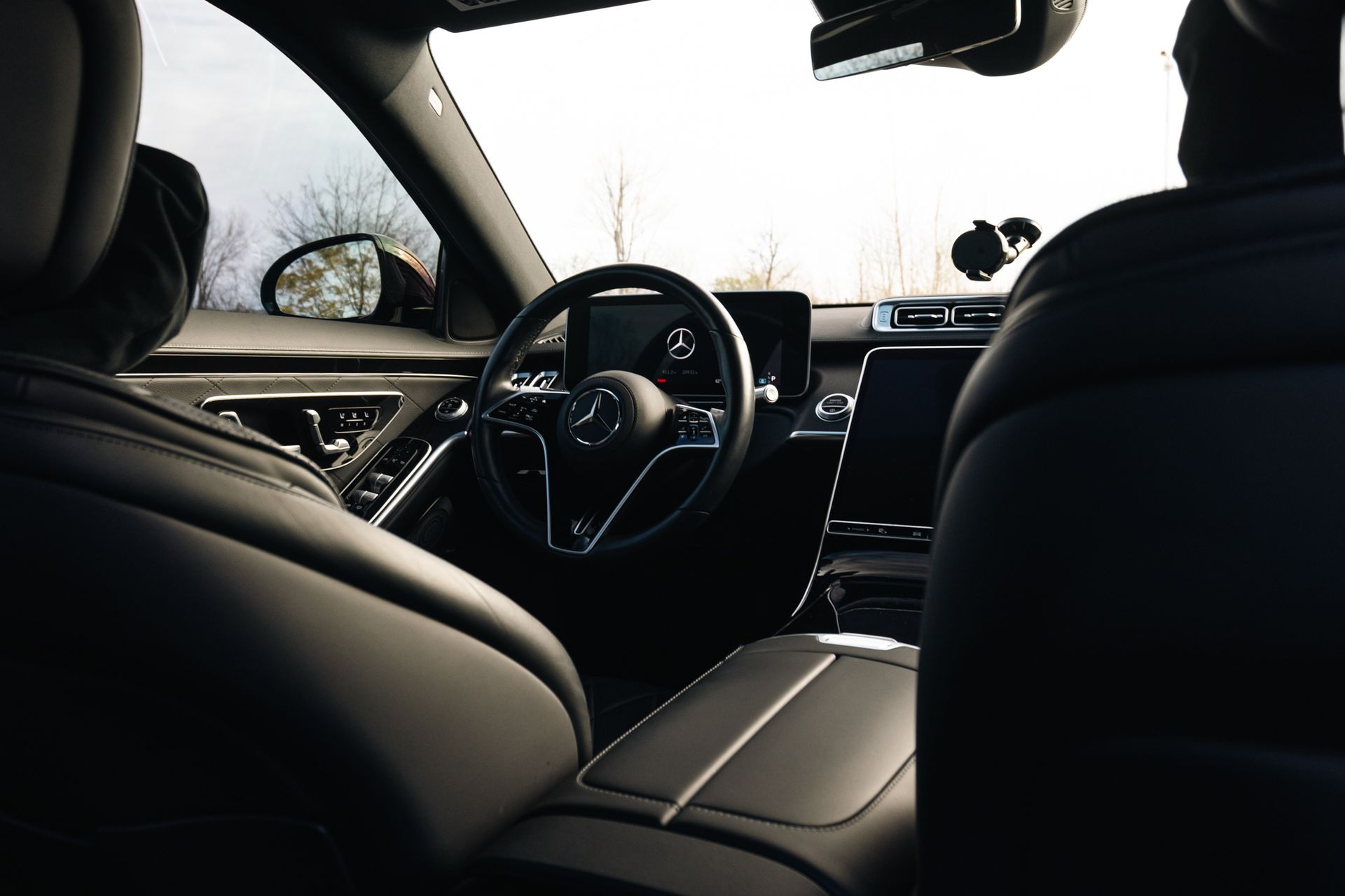 Interior of a modern car, showing the steering wheel, dashboard, and black seats from the back seat.
